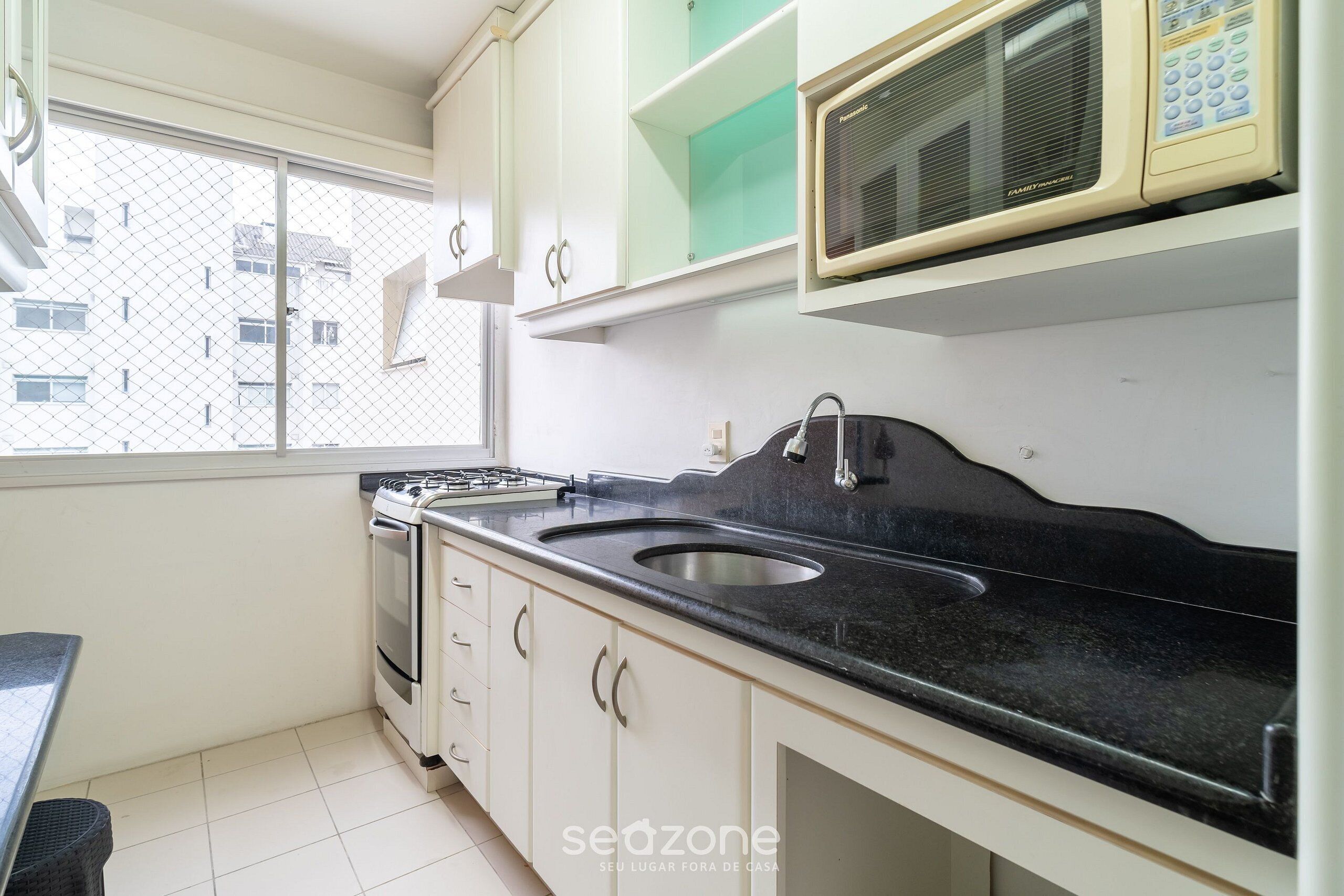 A kitchen with white cabinets, a black countertop, a stove, and a microwave.