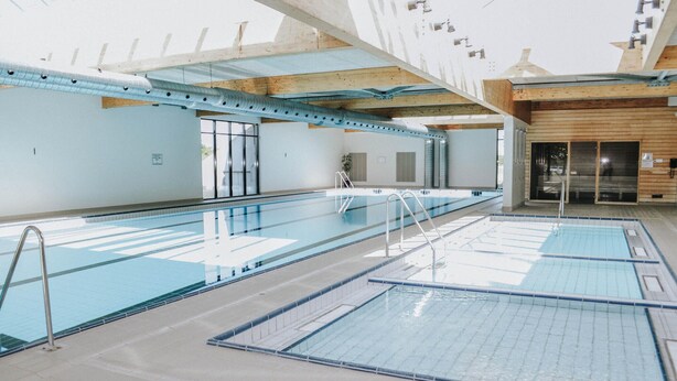 A large indoor swimming pool with multiple lanes, a wooden ceiling, and a glass door entrance. - Beautiful home in Ebeltoft with sauna (Ebeltoft)