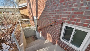 Une façade en briques avec une fenêtre, une main courante en métal et un escalier en béton.