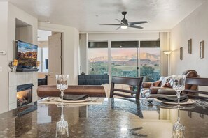 Una sala de estar moderna con un ventanal que ofrece vistas a la montaña, una chimenea y un comedor con mesa y sillas de vidrio.