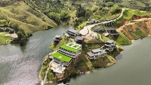 Un hotel a orillas del río con varias edificaciones, una estructura central con techo verde y un paisaje natural circundante.
