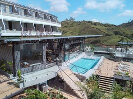 A modern hotel with a rooftop pool, outdoor dining area, and scenic hillside views.