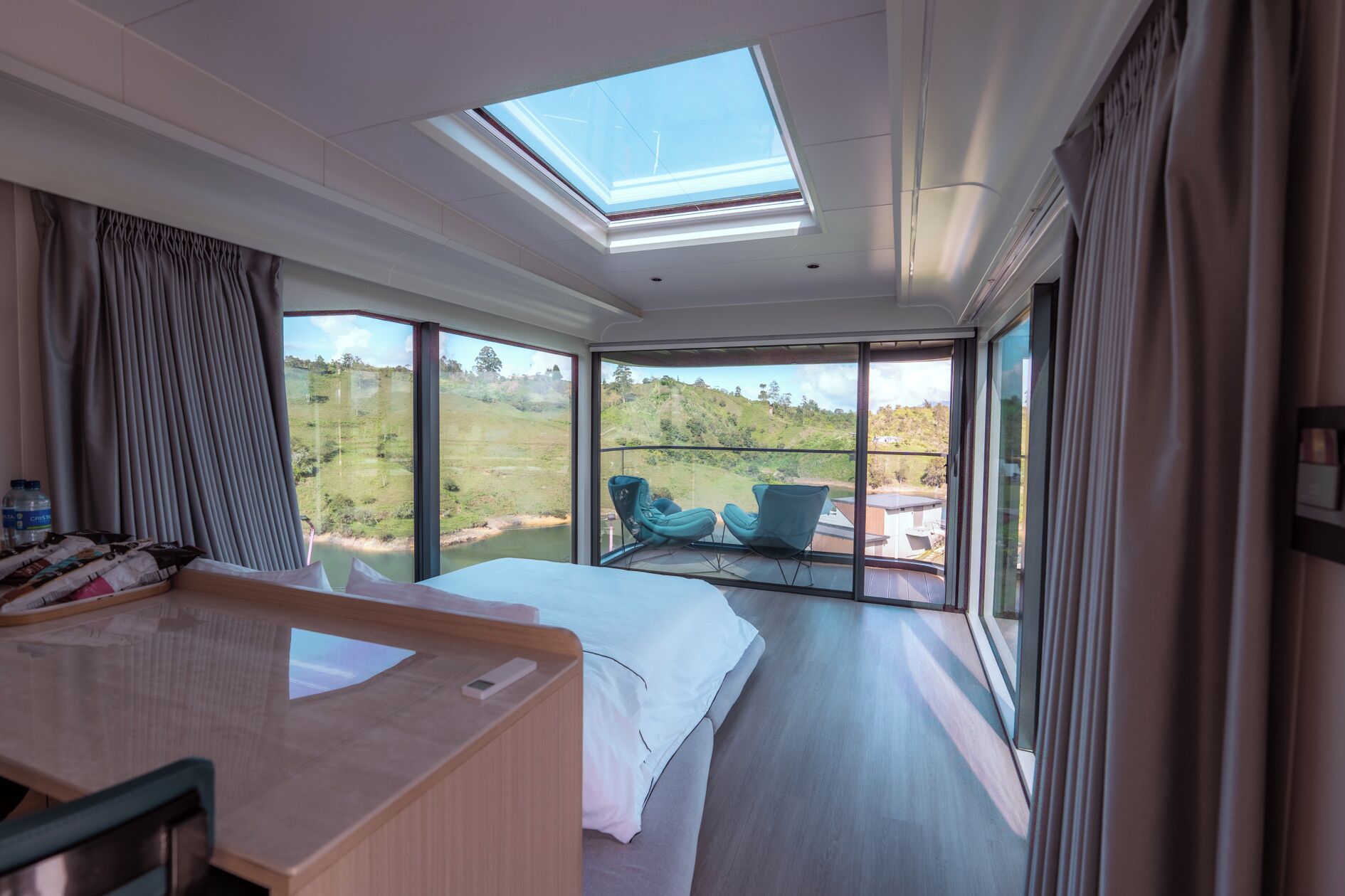 A modern hotel room with a large bed, a desk, and a balcony with chairs.