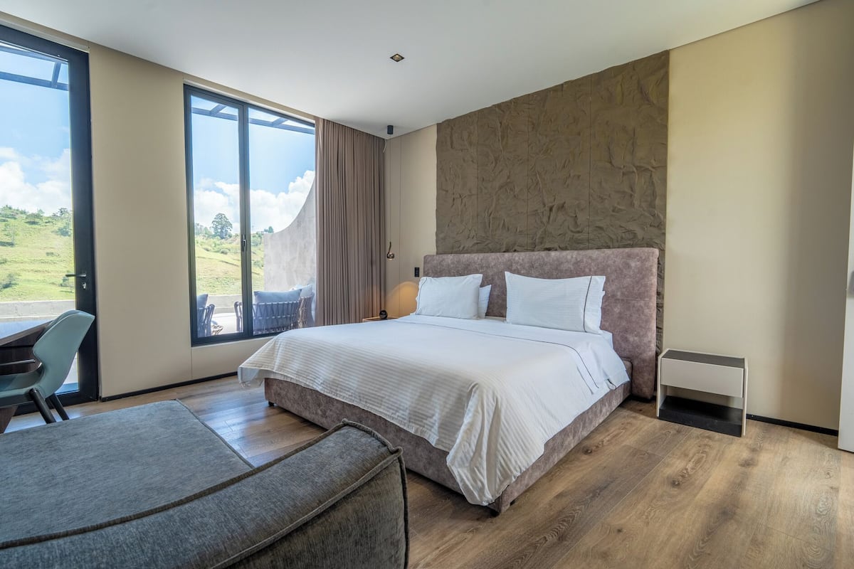 A modern hotel room with a large bed, a desk, and a view of the outdoors.