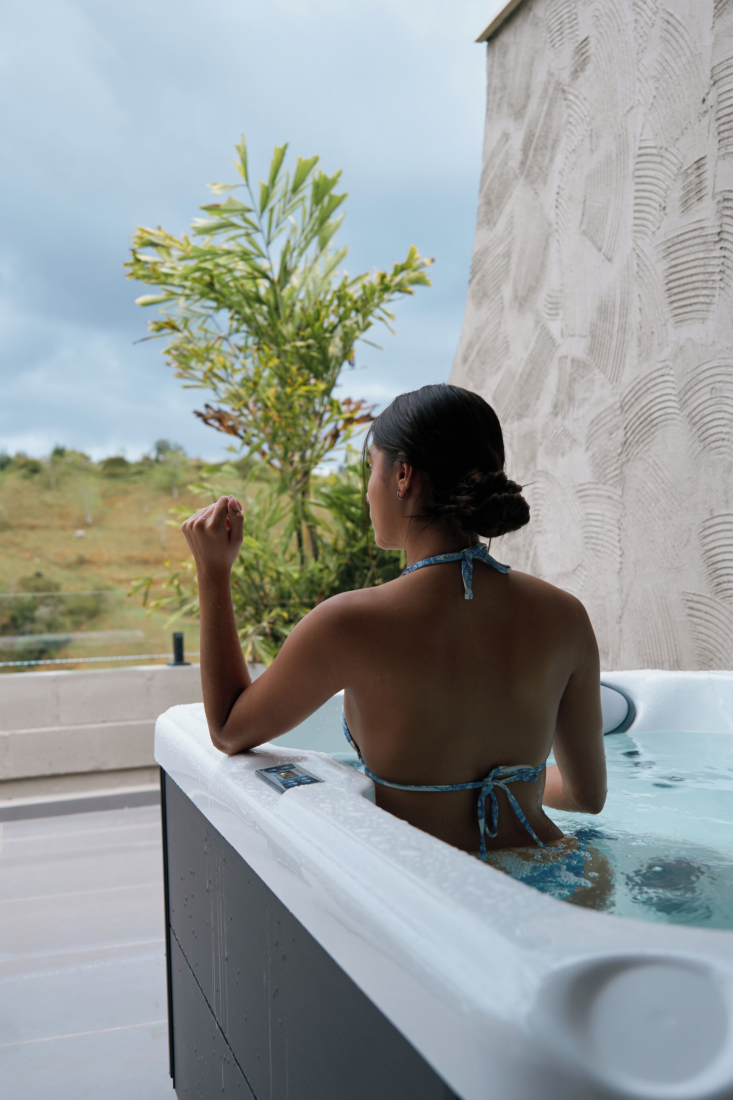 A person in a bathtub with a view of greenery and a building in the background.