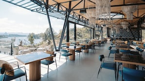 Un restaurante de planta abierta con techos altos, vigas a la vista y lámparas colgantes. Mesas y sillas dispuestas para comer.
