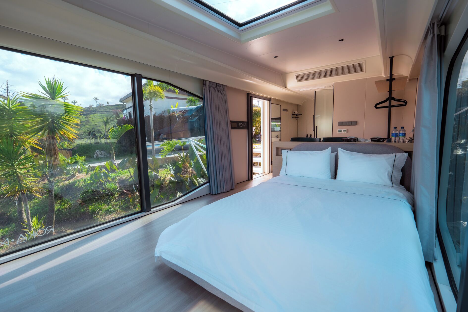 Een moderne hotelkamer met een groot bed, een dakraam en uitzicht op een tropische tuin.