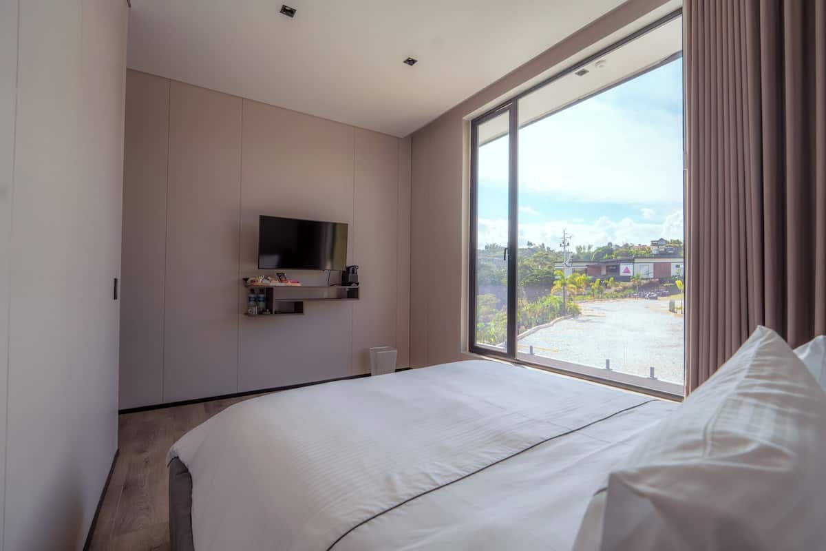 A modern hotel room with a large bed, a mounted TV, and a window with a view of the outside.