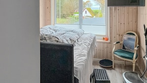 Una camera da letto con un letto, una sedia, un tavolino e una finestra vista casa e alberi.
