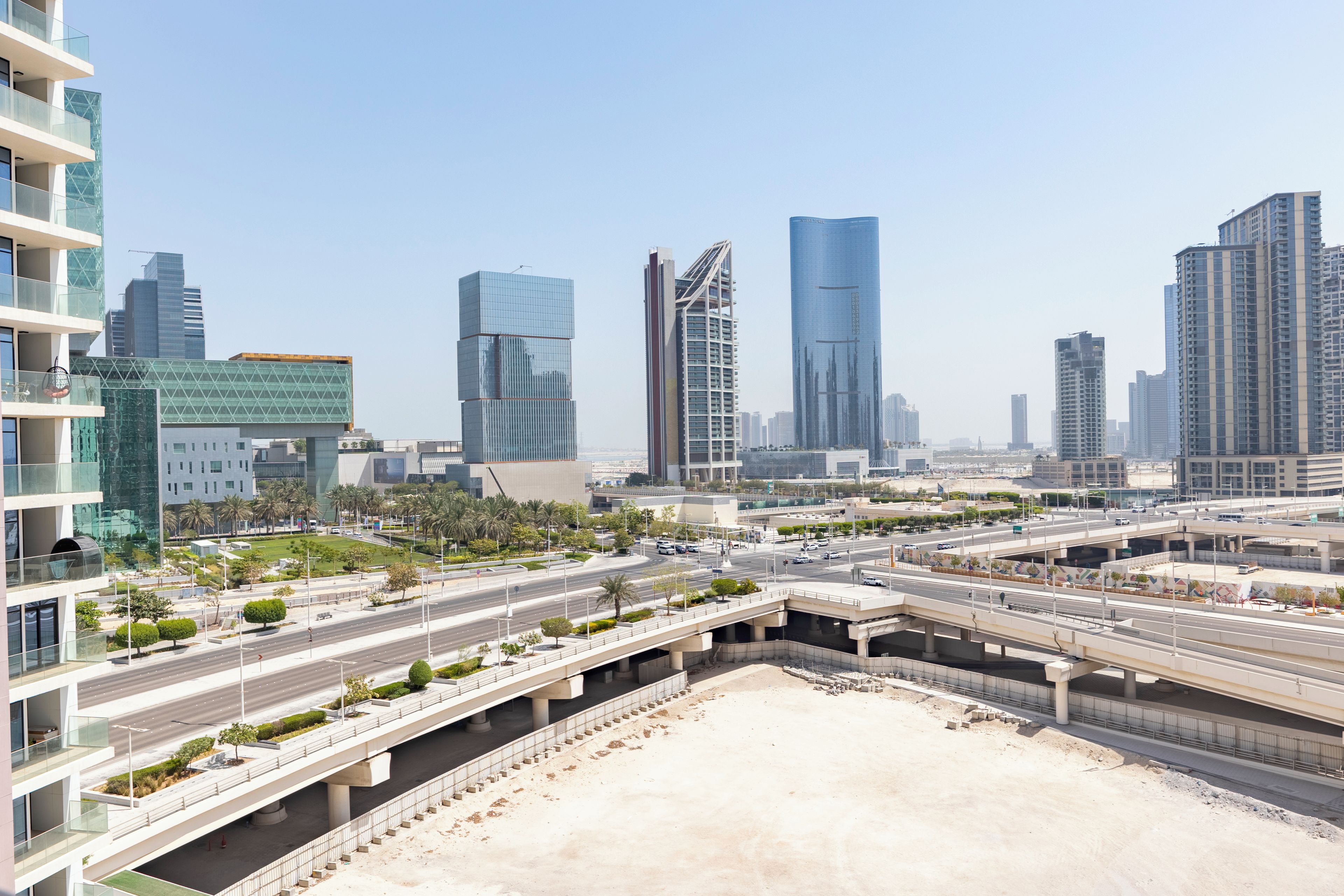 A modern cityscape with high-rise buildings, a multi-level highway interchange, and landscaped areas.