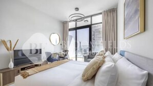 Ein modernes Hotelzimmer mit einem großen Bett, einem Schreibtisch, einem Sessel, einem Fernseher und einem großen Fenster mit Vorhängen.