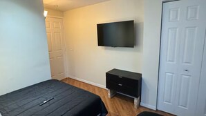 A bedroom with a loft bed, a flat-screen TV mounted on the wall, a bedside table, and a door.