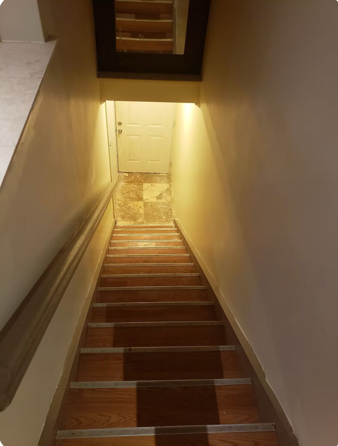 Una escalera de madera con una puerta blanca al final, que da a una zona de descanso.