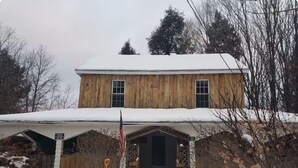 A two-story wooden house with a snow-covered roof and a front porch.