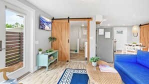 Una sala de estar moderna con un sofá azul, una puerta corredera de madera, una zona de cocina y una mesa de comedor con sillas.
