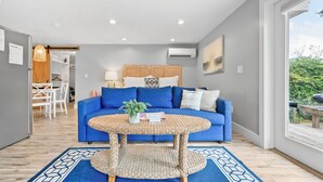 Una sala de estar moderna con un sofá azul, una mesa de centro redonda de fibra natural y vistas a zonas verdes al exterior.