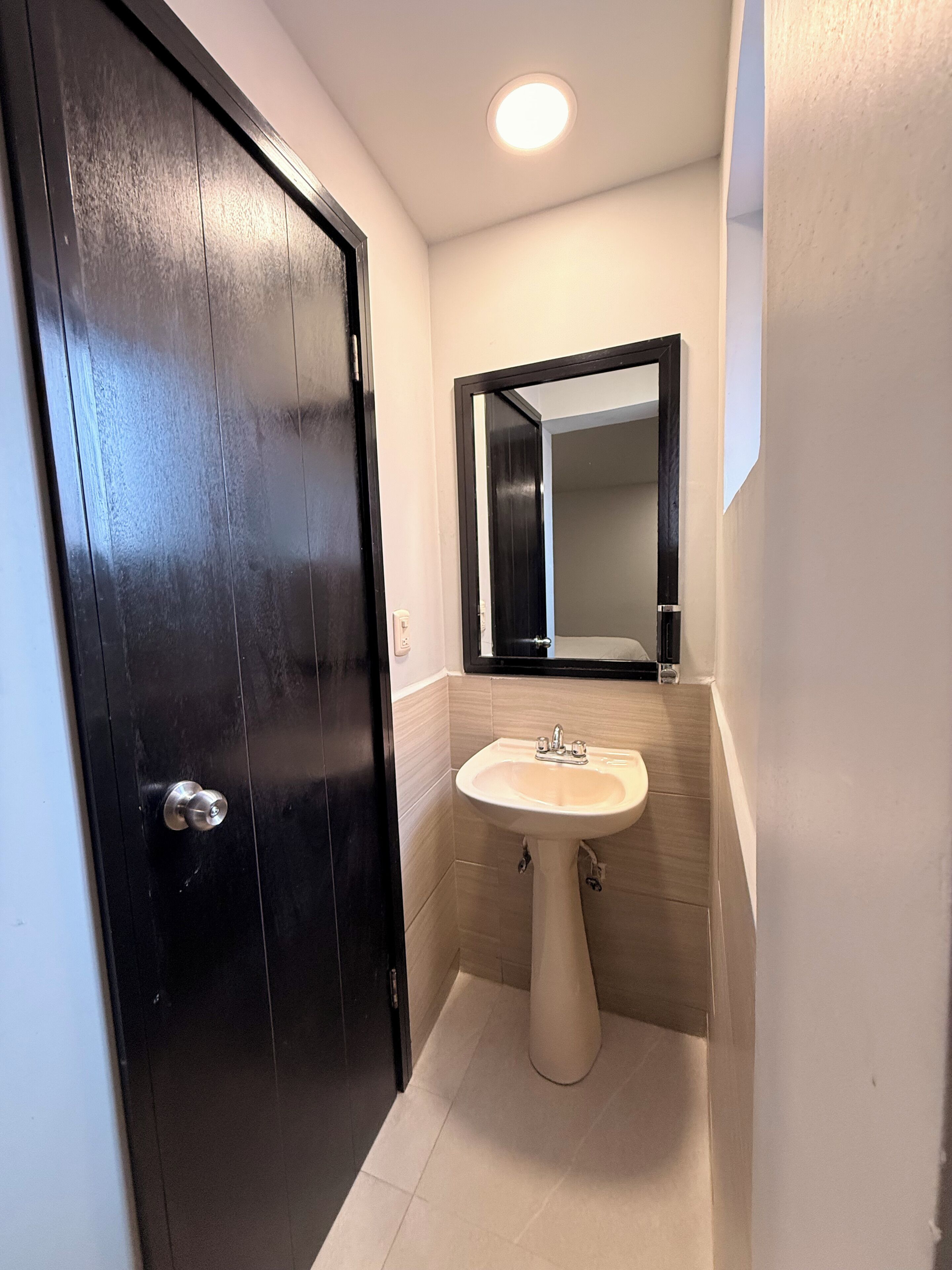 A bathroom with a black door, a white sink, and a mirror above it.