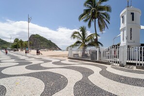 A tiled walkway with palm trees and a beach in the background. - Loft com Ar Condicionado e Wi-fi a 140m da Praia (Rio de Janeiro)