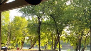 Un espace extérieur abrité, doté d’un sol en gravier, entouré d’arbres et bordé par un plan d’eau.