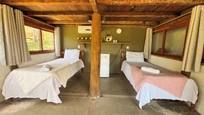 A room with two beds, a small refrigerator, a shelf with cups and a mirror, and a window with curtains. - Bangal Beira da Lagoa com Acesso Direto Praia (Prado)
