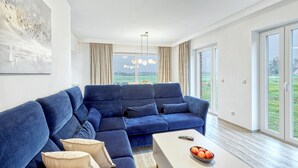 Ein modernes Wohnzimmer mit einem blauen Ecksofa, einem weißen Couchtisch mit Äpfeln und einem Gemälde an der Wand.