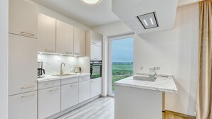 Eine moderne Küche mit weißen Schränken, einer Marmorarbeitsplatte und Blick auf ein grünes Feld durch ein großes Fenster.