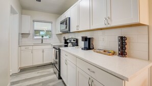 Una cocina moderna con armarios blancos, microondas, cafetera y hervidor.