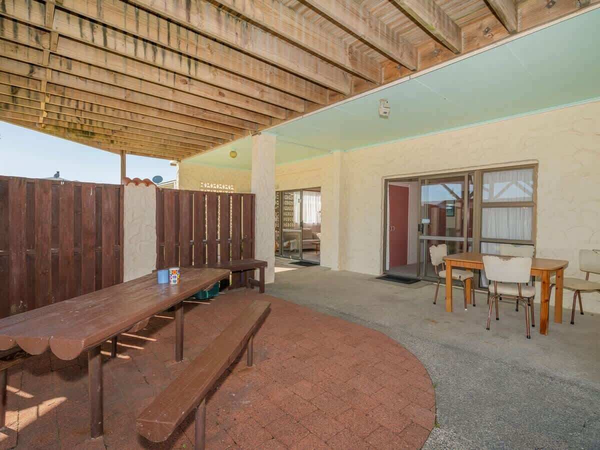 An outdoor patio with a wooden table and chairs, a covered seating area, and a view of a building in the background.
