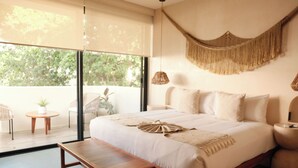 Ein Schlafzimmer mit einem großen Bett, einer Bank, einem kleinen Tisch und einer Wanddekoration aus Makramee.