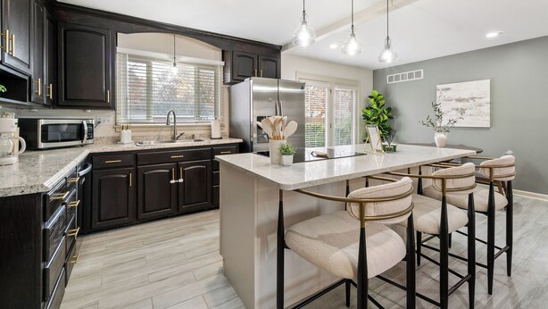 A modern kitchen with dark cabinetry, a central island with bar stools, a refrigerator, and a microwave.