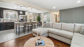 A modern living room with a sectional sofa, a round coffee table, and a kitchen area with bar stools.