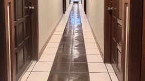 A hotel hallway with dark wooden doors, white tiled flooring, and a fire extinguisher mounted on the wall. - Hotel Mirage Diagonal (Matamoros)