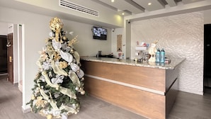A modern reception area with a wooden reception desk, a large Christmas tree, and a mounted television. - Hotel Mirage Diagonal (Matamoros)