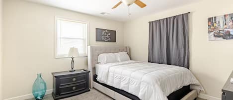 A neutral bedroom with an upholstered bed, ceiling fan, and carpeted flooring.