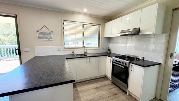 A kitchen with a large island, a gas stove, a sink, and white cabinets. - Tanjil Cottage | Relaxing Coastal Stay (Lakes Entrance)