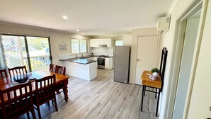 A modern kitchen with a central island, wooden dining table, and chairs. - Tanjil Cottage | Relaxing Coastal Stay (Lakes Entrance)