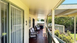 A covered porch with a grill, outdoor seating, and a view of the backyard. - Tanjil Cottage | Relaxing Coastal Stay (Lakes Entrance)