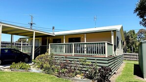 A two-story building with a covered porch and a fenced yard. - Tanjil Cottage | Relaxing Coastal Stay (Lakes Entrance)