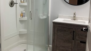 A modern bathroom with a glass-enclosed shower, a wooden vanity, and a round mirror.