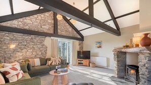 A cozy living room with a stone wall, a fireplace, and a television. - Royal Oak Barn - Cartmel, Sleeps 8! (NEW) (Cartmel)
