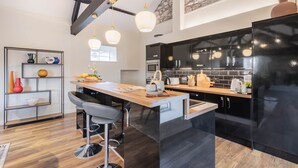 A modern kitchen with a central island, bar stools, a black refrigerator, and a stone accent wall. - Royal Oak Barn - Cartmel, Sleeps 8! (NEW) (Cartmel)
