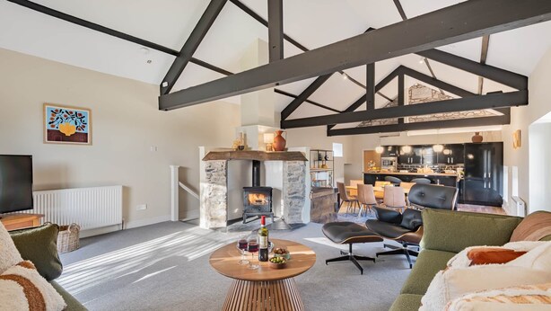 A modern living room with a stone fireplace, a dining area, and a kitchen in the background. - Royal Oak Barn - Cartmel, Sleeps 8! (NEW) (Cartmel)