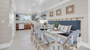 A modern kitchen with white cabinetry, a dining area with blue and white patterned chairs, and a blue cushioned bench. - “Aura” 5min to beach- sleeps 20- pool with waterfall and fire features (Bradenton)