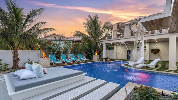 A swimming pool with lounge chairs, a fire feature, and a view of a sunset. - “Aura” 5min to beach- sleeps 20- pool with waterfall and fire features (Bradenton)