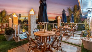 An outdoor seating area with tables and chairs, surrounded by stone pillars with torches, and umbrellas. - “Aura” 5min to beach- sleeps 20- pool with waterfall and fire features (Bradenton)