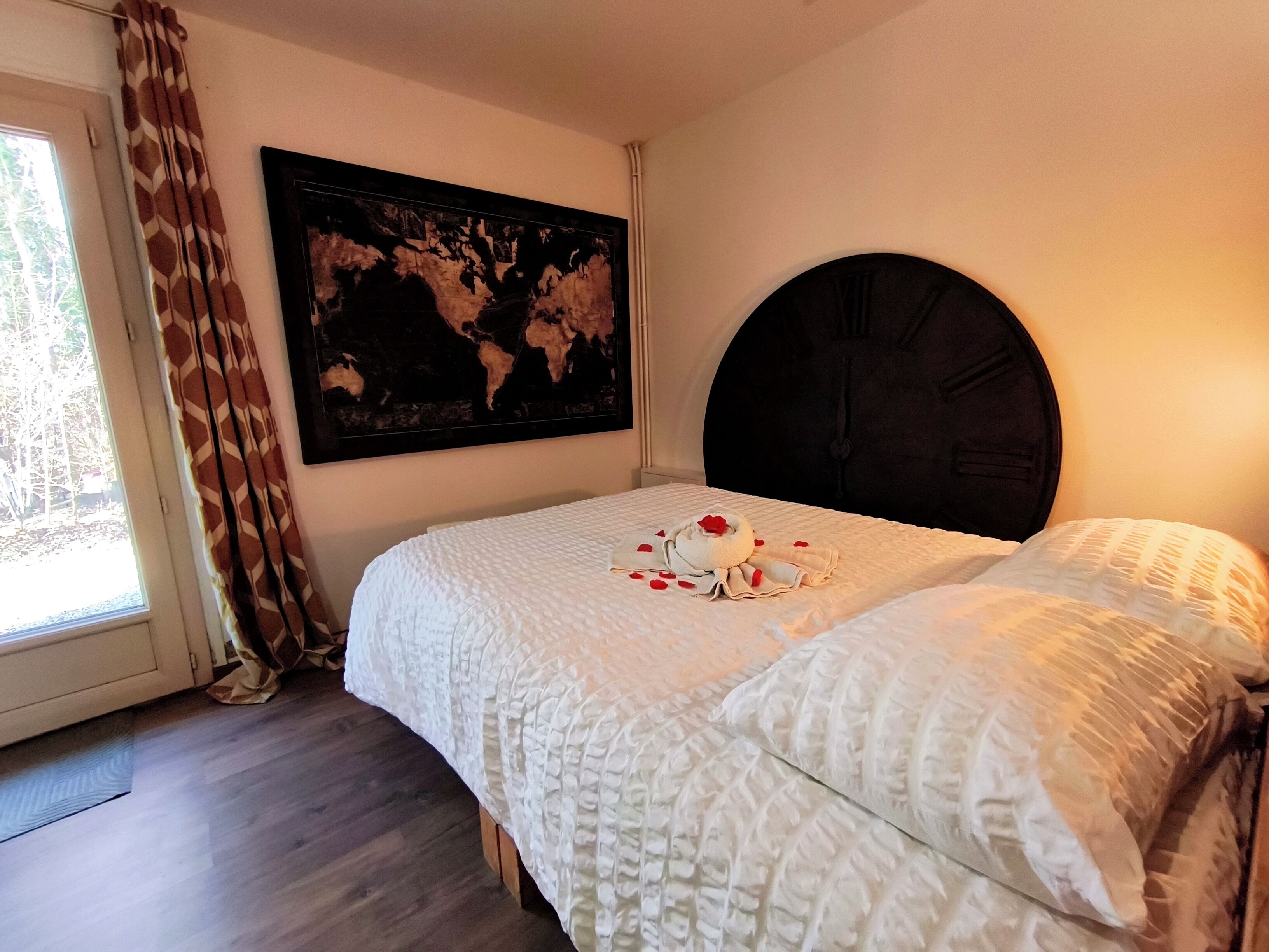 Une chambre avec un grand lit, une carte du monde accrochée au mur et une fenêtre avec des rideaux.