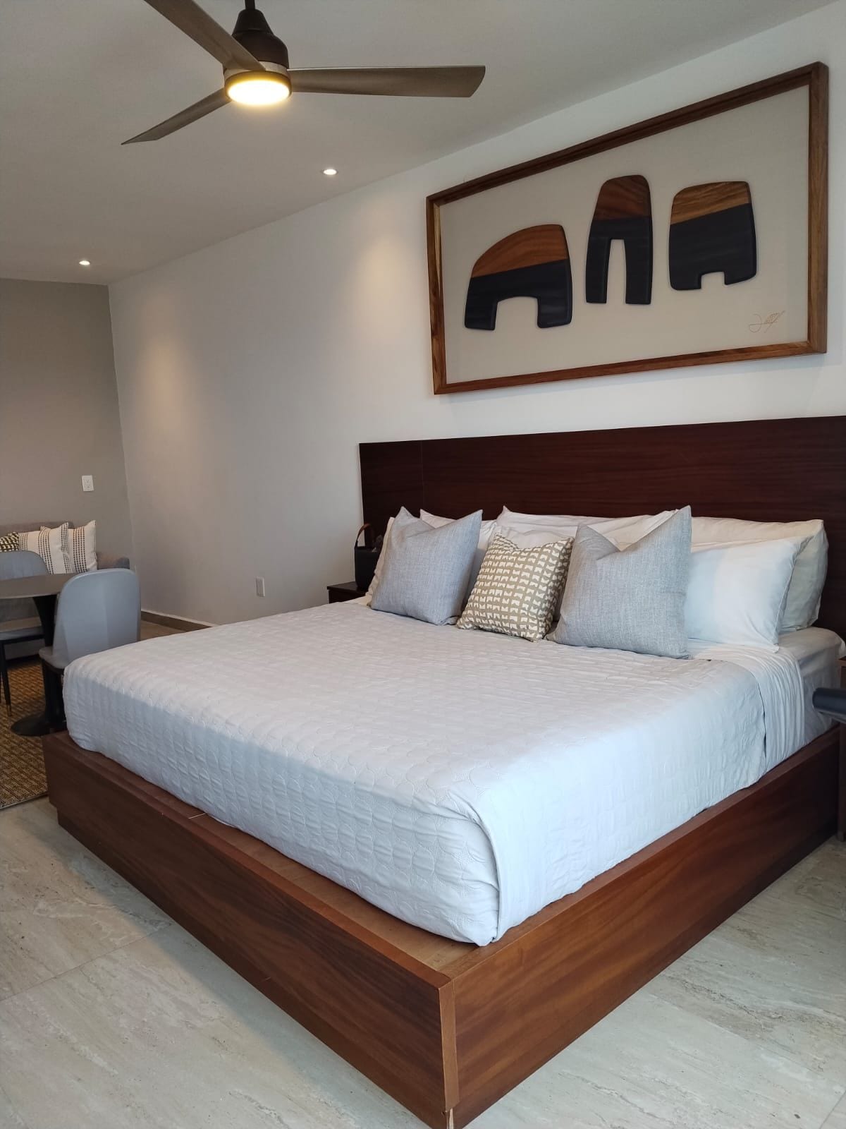 A bedroom with a large bed, a ceiling fan, and a wall-mounted artwork.