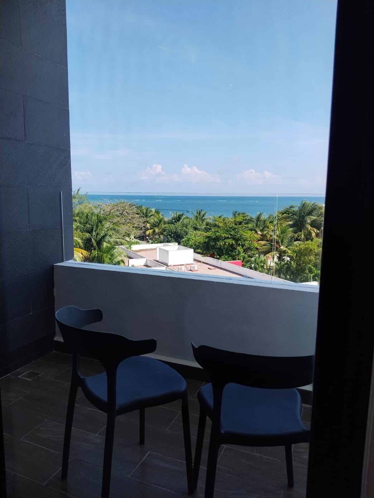 A balcony with two chairs and a view of the ocean and greenery.