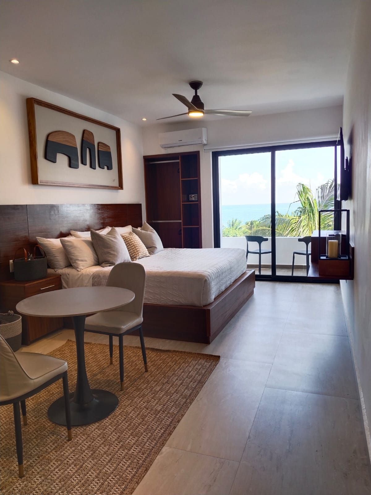 Een slaapkamer met een bed, een ronde tafel en een stoel. Er is een groot raam met uitzicht op de oceaan.