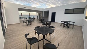 Eine großzügige Dachterrasse mit mehreren Tischen und Stühlen, Blick auf das Meer und modernes architektonisches Design.